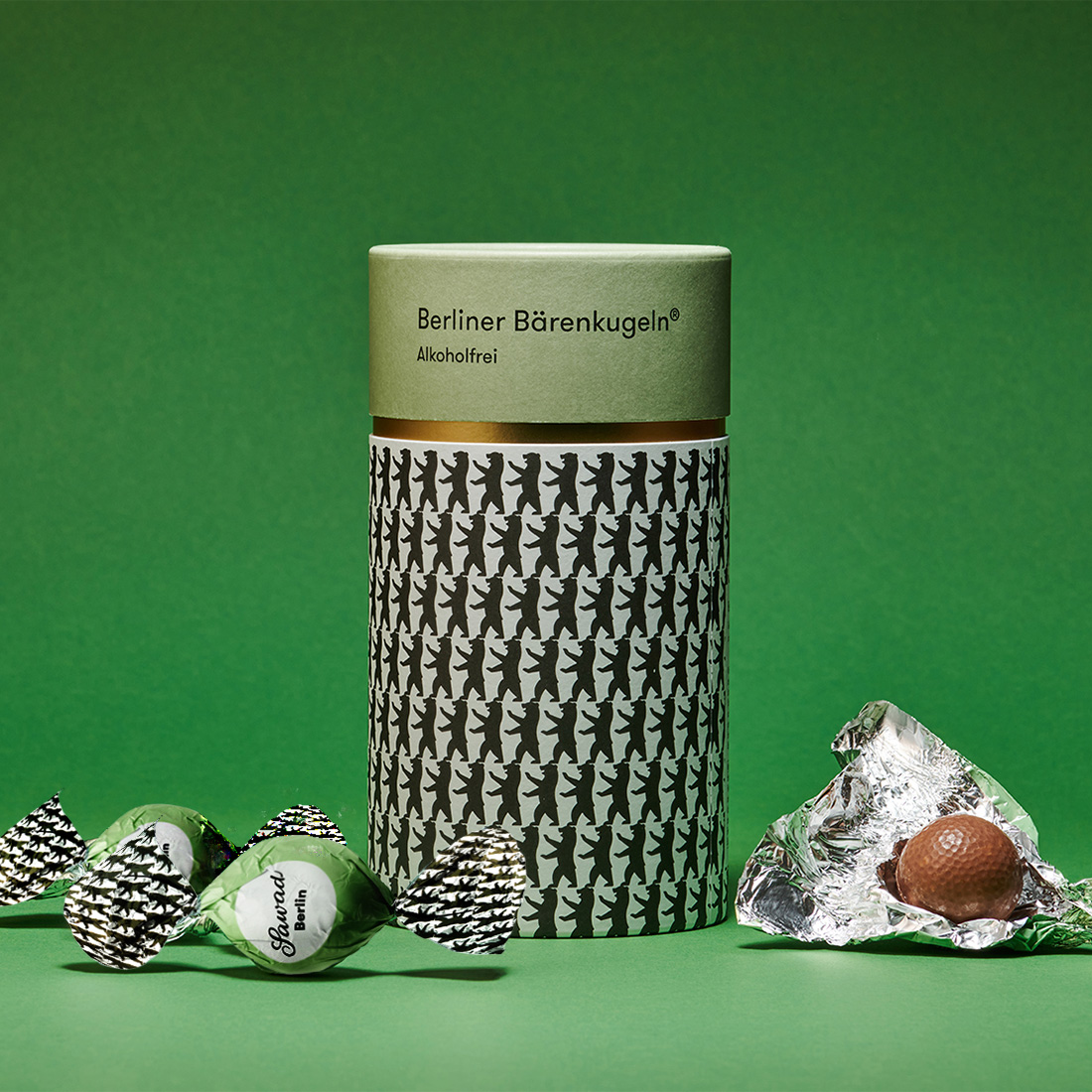 Stimmungsbild: Berliner Bärenkugel Dose vor grünem Hintergrund mit drei Bärenkugeln neben der Dose Stimmungsbild: Berliner Bärenkugel Dose vor grünem Hintergrund mit drei Bärenkugeln neben der Dose