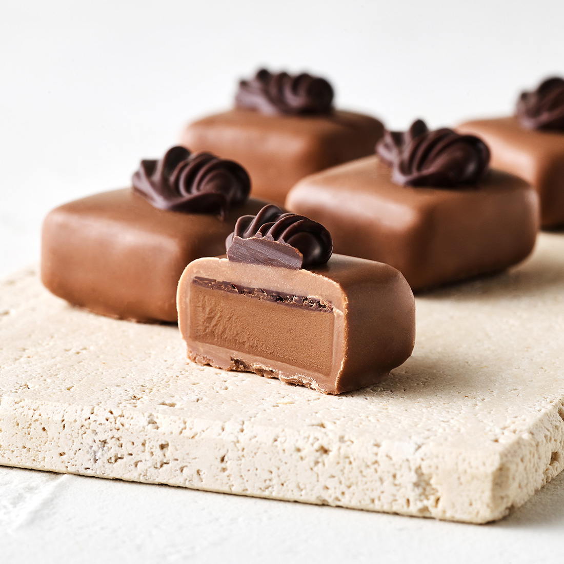 Stimmungsbild: Nussbitter-Nougat Trüffel in Vollmilchschokolade mit Zarbitterschokoladen-Dekor appetitlich angeschnitten Stimmungsbild: Nussbitter-Nougat Trüffel in Vollmilchschokolade mit Zarbitterschokoladen-Dekor appetitlich angeschnitten