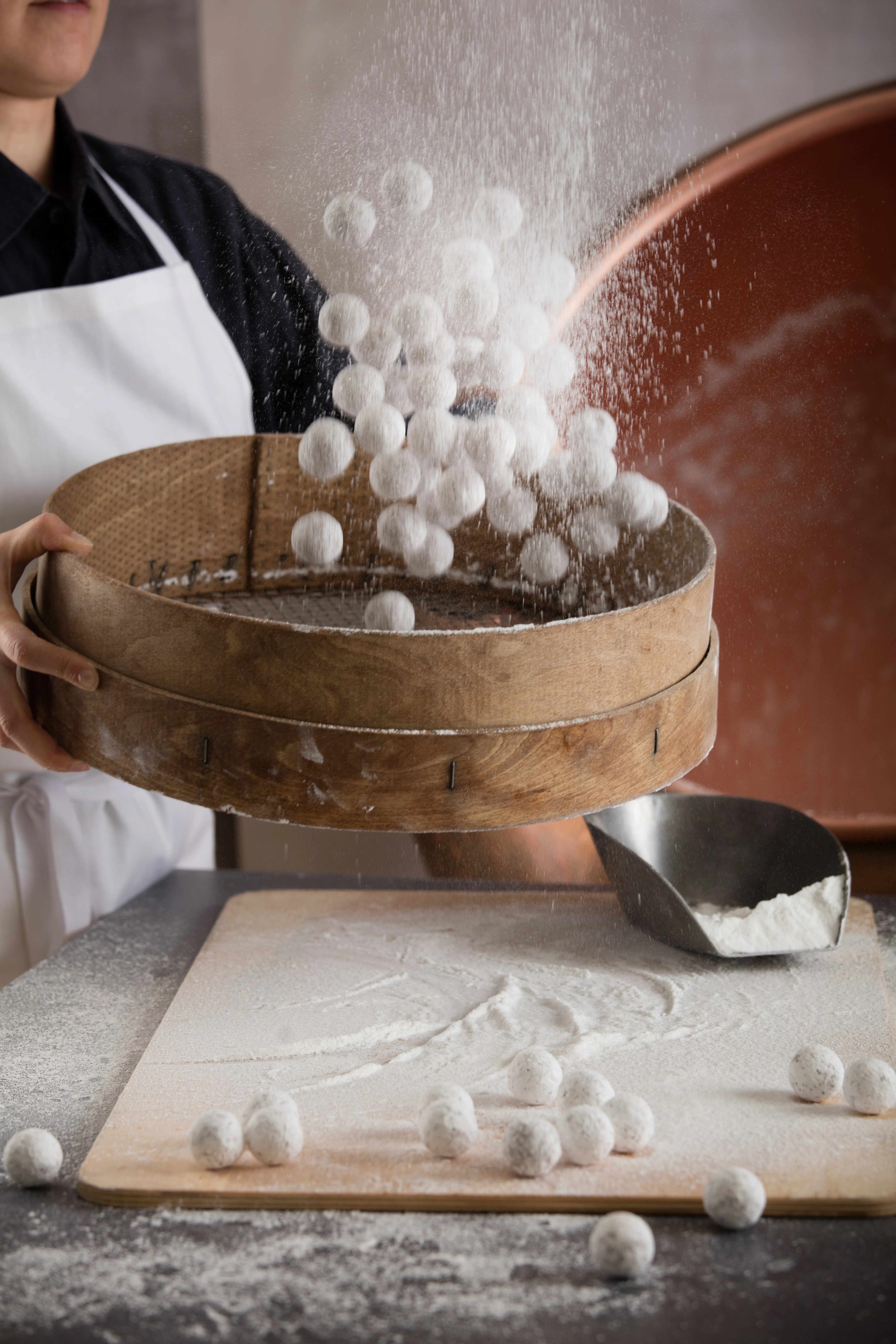 Eine Person bepudert Pralinen mit Puderzucker mithilfe eines großen Siebs