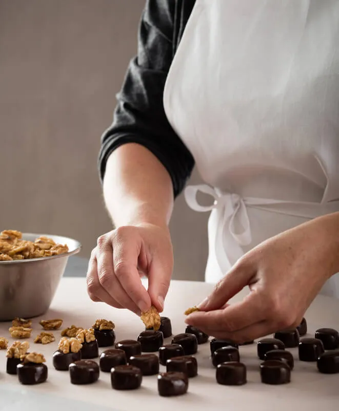 Eine Frau legt halbe Walnüsse auf Marzipan Pralinen