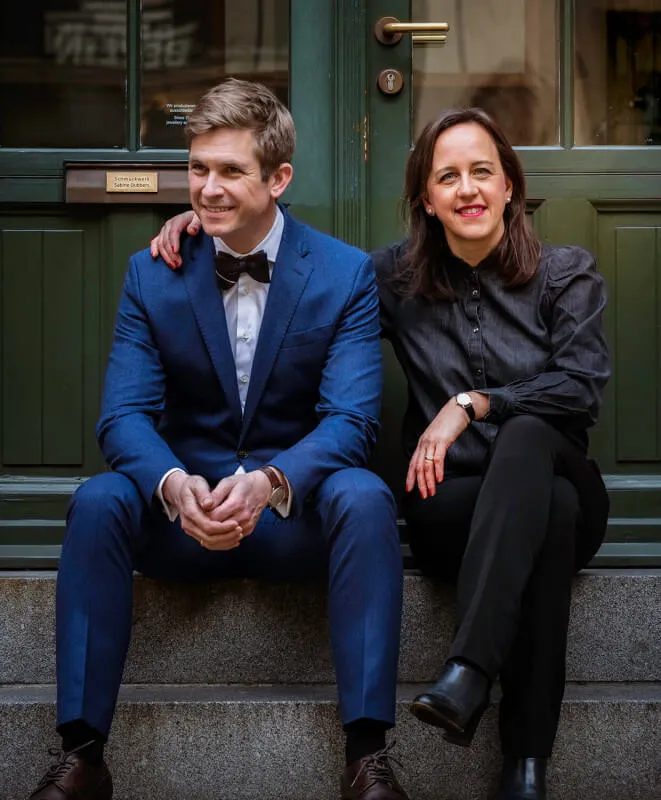 Melanie und Benno Hübel sitzen nebeneinander auf Stufen vor einer grünen Tür