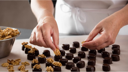 Produktionsaufnahme: Halbe Walnüsse werden von Hand auf Walnuss Marzipan Pralinen gelegt Produktionsaufnahme: Halbe Walnüsse werden von Hand auf Walnuss Marzipan Pralinen gelegt