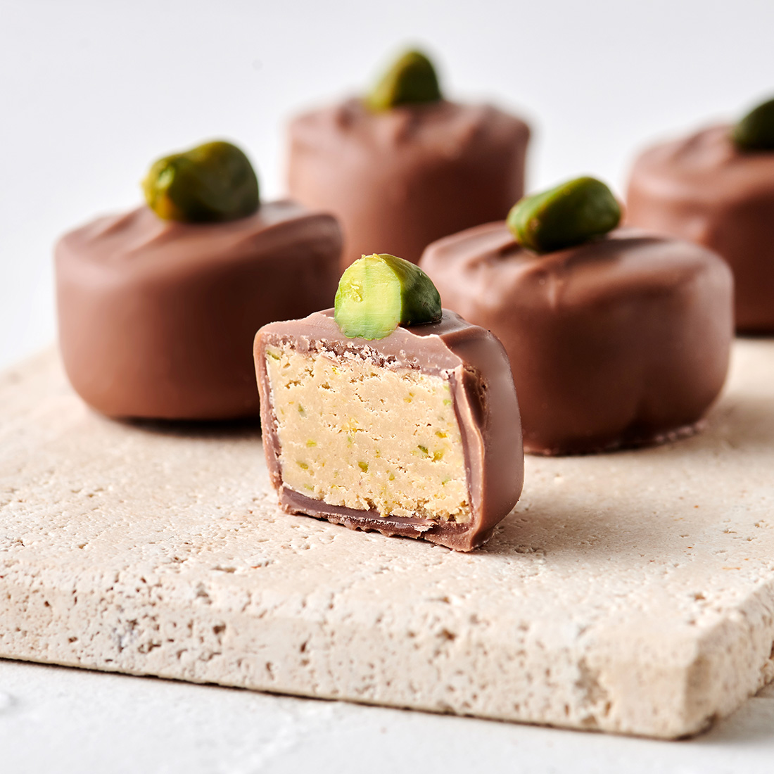 Stimmungsbild: Pistazien-Nougat Praline mit Vollmilchschokolade überzogen und aufgesetzter Pistazie dekorativ angeschnitten Stimmungsbild: Pistazien-Nougat Praline mit Vollmilchschokolade überzogen und aufgesetzter Pistazie dekorativ angeschnitten