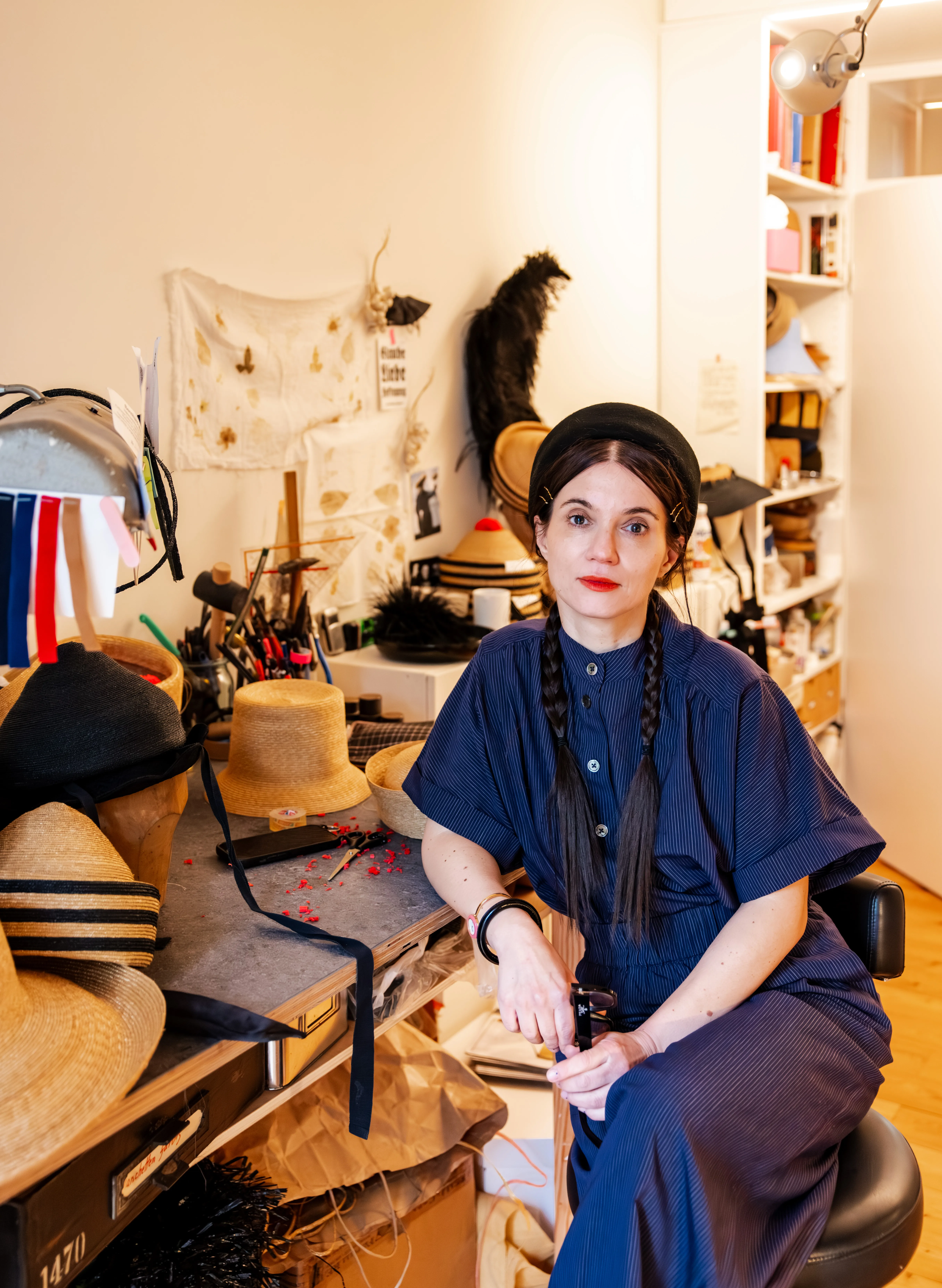 Susanne Stein sitzt in ihrem Atelier, blickt in die Kamera und stützt sich auf ihren Schreibtisch auf.