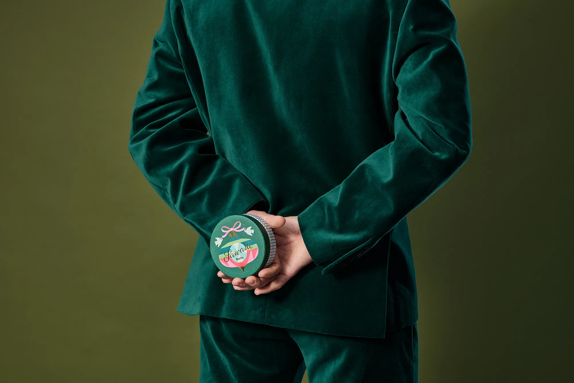 Mann im grünen Jacket hält eine Runddose Schmuckstück hinter seinem Rücken
